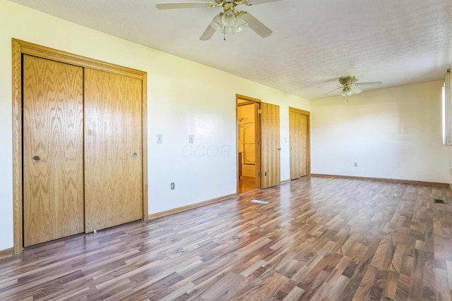 unfurnished bedroom with hardwood / wood-style floors, ceiling fan, and two closets