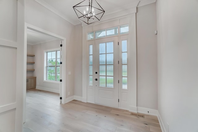 foyer entrance with light wood-type flooring, ornamental molding, and an inviting chandelier