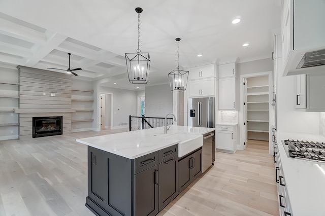 kitchen featuring stainless steel appliances, sink, a center island with sink, white cabinetry, and hanging light fixtures