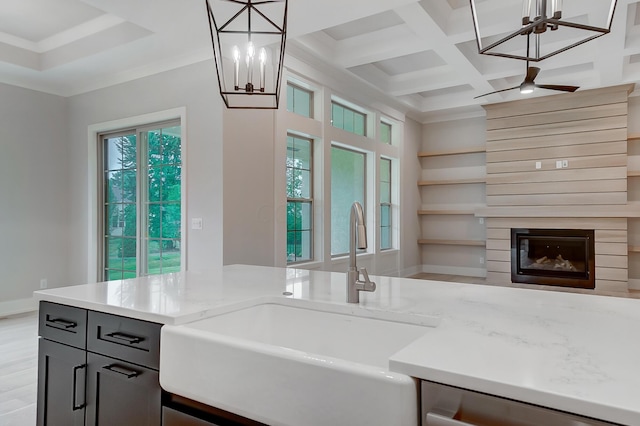 kitchen featuring light stone countertops, dishwasher, coffered ceiling, pendant lighting, and a fireplace