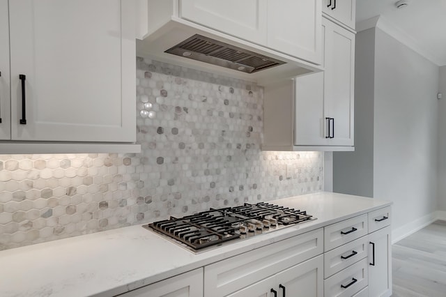 kitchen featuring stainless steel gas cooktop, premium range hood, decorative backsplash, white cabinets, and light wood-type flooring