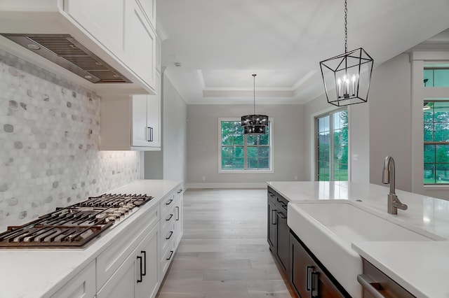 kitchen with custom range hood, sink, decorative light fixtures, an inviting chandelier, and white cabinetry