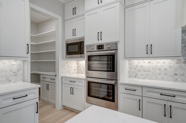 kitchen with backsplash, white cabinetry, double oven, and built in microwave