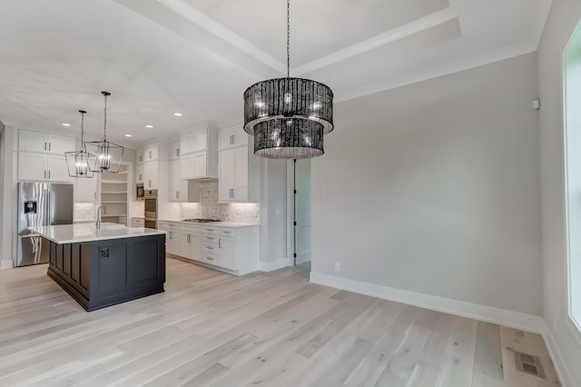 kitchen with decorative backsplash, light wood-type flooring, stainless steel appliances, decorative light fixtures, and an island with sink