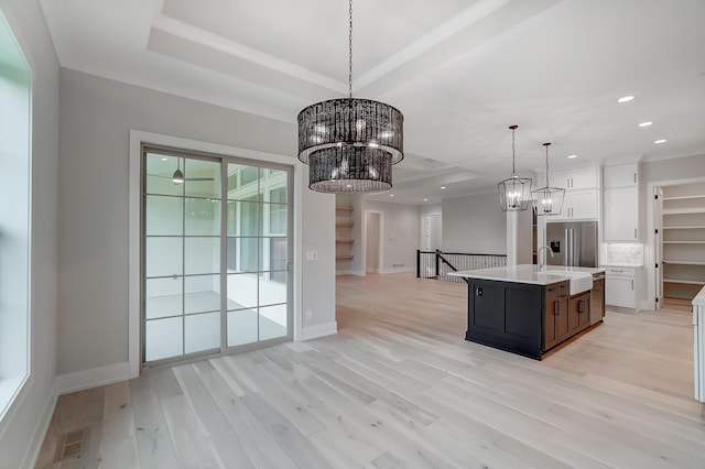 kitchen featuring decorative light fixtures, light hardwood / wood-style floors, white cabinetry, and a kitchen island with sink