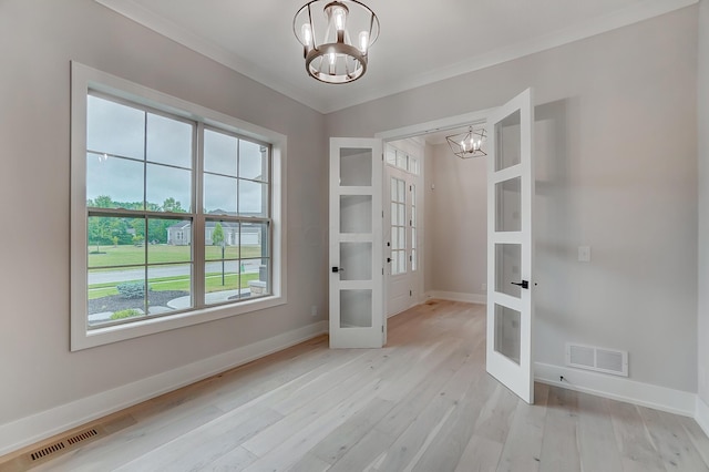 unfurnished dining area featuring a chandelier, light wood-type flooring, ornamental molding, and french doors