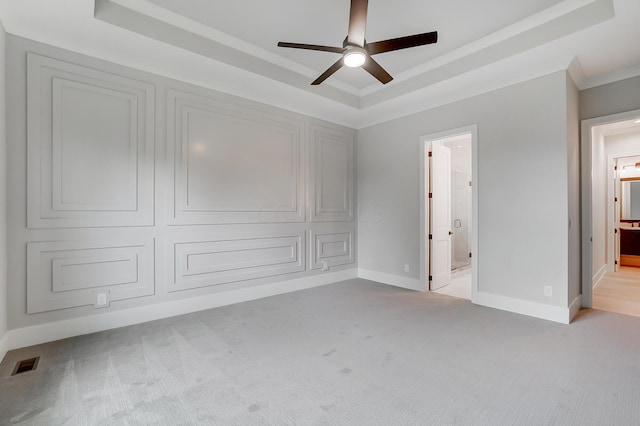 unfurnished bedroom with light carpet, a tray ceiling, ensuite bath, and ceiling fan