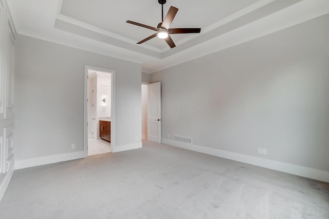 unfurnished bedroom featuring connected bathroom, ceiling fan, crown molding, a tray ceiling, and light carpet