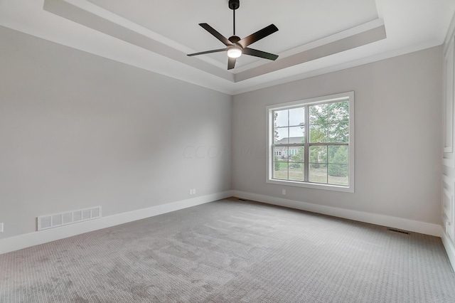 empty room with a tray ceiling, ceiling fan, carpet flooring, and ornamental molding