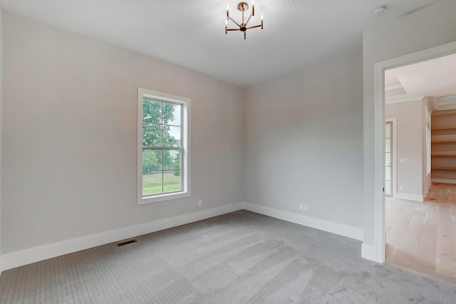 carpeted spare room with an inviting chandelier