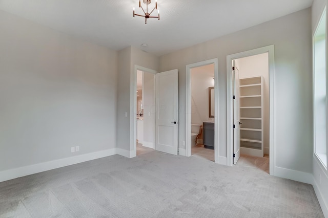 unfurnished bedroom featuring a closet, light colored carpet, a spacious closet, and ensuite bath