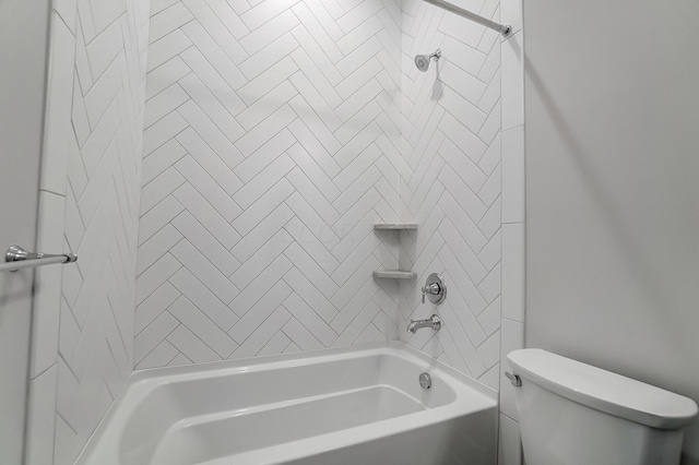 bathroom featuring tiled shower / bath combo and toilet