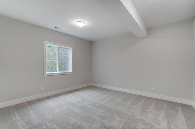 spare room featuring beamed ceiling and light colored carpet