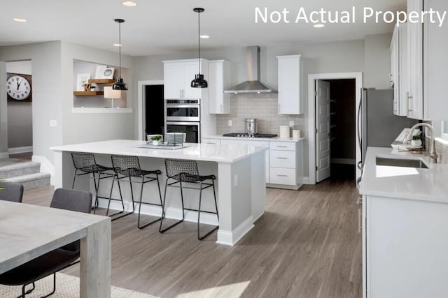 kitchen featuring white cabinets, wall chimney exhaust hood, hanging light fixtures, and appliances with stainless steel finishes