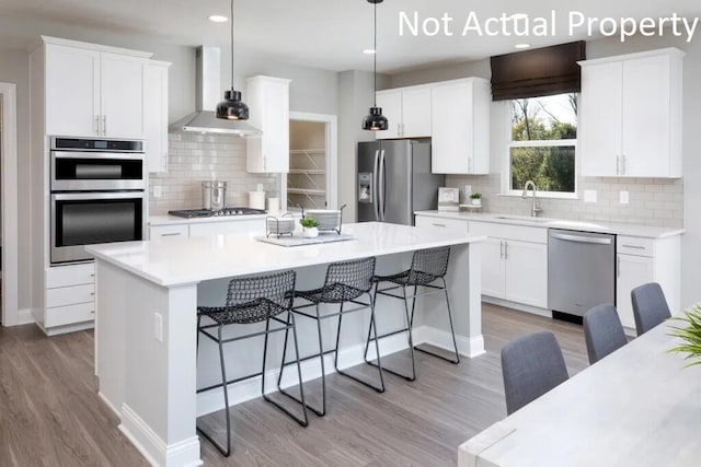 kitchen featuring stainless steel appliances, wall chimney range hood, a center island, white cabinetry, and hanging light fixtures