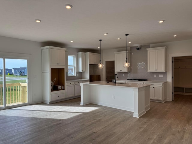 kitchen with a healthy amount of sunlight, light wood-type flooring, white cabinetry, and an island with sink