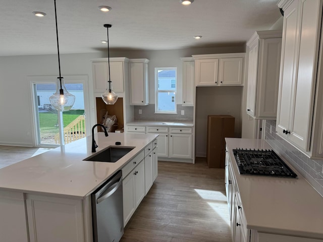 kitchen with sink, stainless steel dishwasher, pendant lighting, a center island with sink, and light wood-type flooring