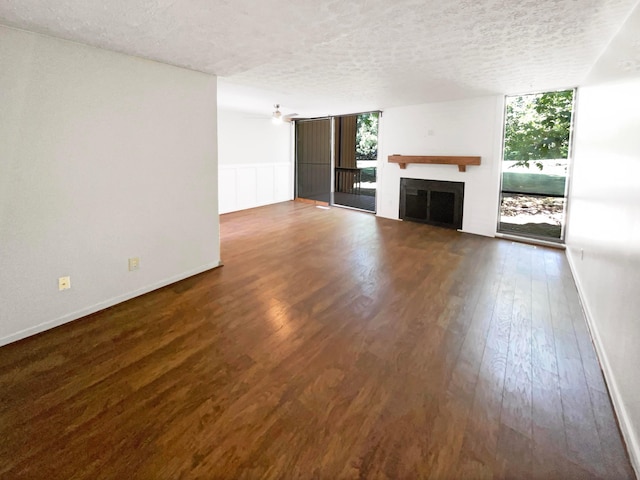 unfurnished living room with ceiling fan, dark wood-type flooring, a textured ceiling, and a wall of windows