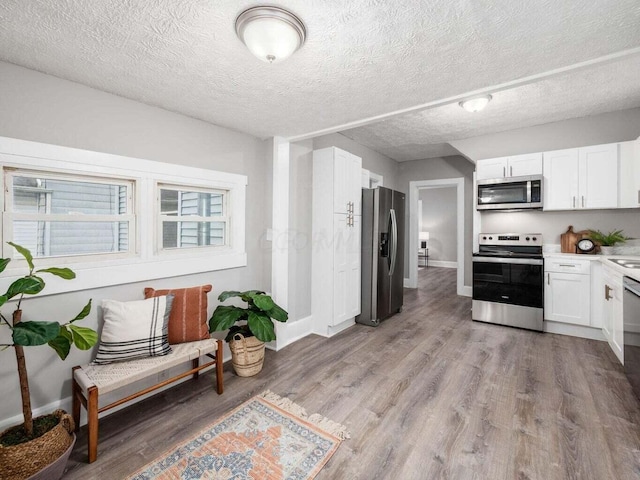 kitchen with white cabinets, a textured ceiling, stainless steel appliances, and light hardwood / wood-style flooring