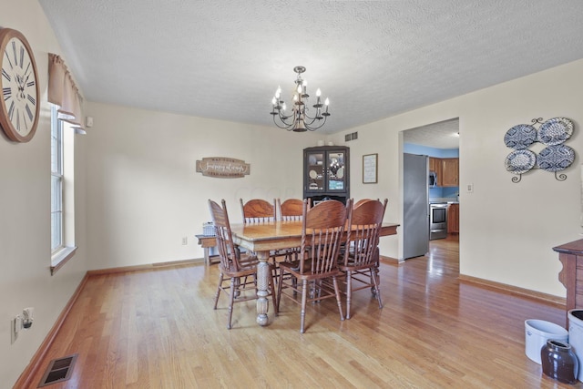 dining area featuring light wood-type flooring, a textured ceiling, and a chandelier