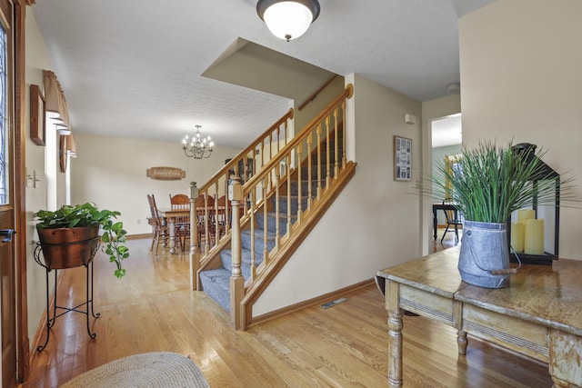 staircase with wood-type flooring, a textured ceiling, and a chandelier