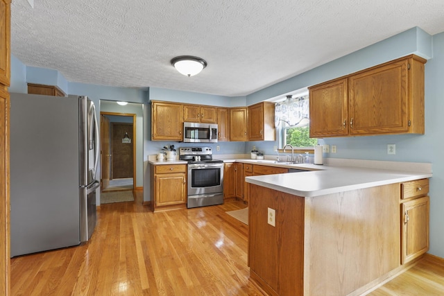 kitchen with kitchen peninsula, light hardwood / wood-style floors, a textured ceiling, and appliances with stainless steel finishes