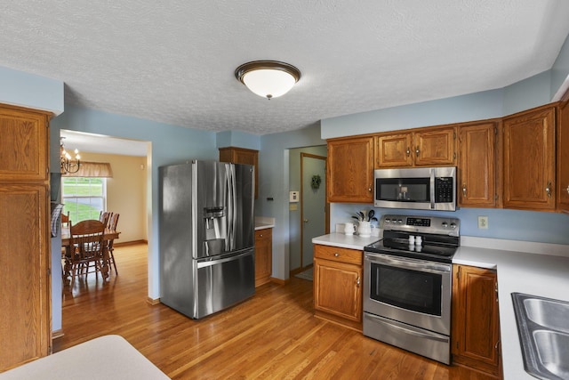 kitchen featuring an inviting chandelier, stainless steel appliances, a textured ceiling, and light hardwood / wood-style floors