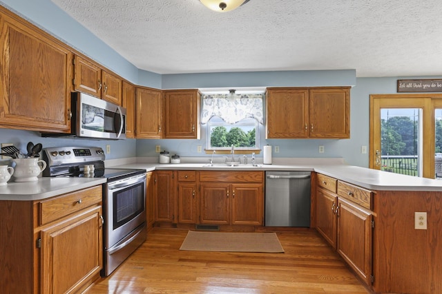 kitchen featuring sink, light hardwood / wood-style flooring, a textured ceiling, kitchen peninsula, and stainless steel appliances