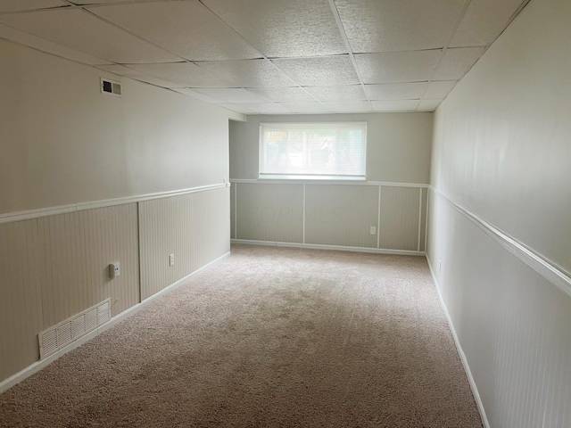 carpeted spare room with a drop ceiling and wood walls