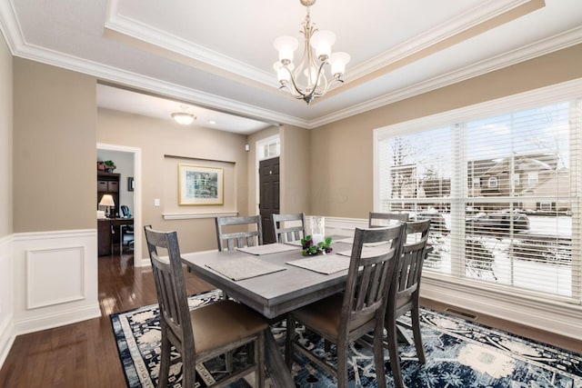 dining space with a raised ceiling, ornamental molding, dark hardwood / wood-style floors, and an inviting chandelier