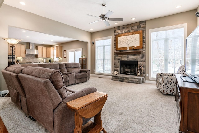 carpeted living room with ceiling fan and a stone fireplace