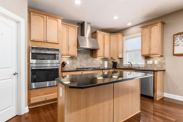 kitchen with stainless steel appliances, a center island, dark stone counters, light brown cabinetry, and wall chimney range hood