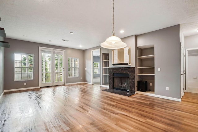 unfurnished living room with hardwood / wood-style flooring, built in features, a textured ceiling, and a high end fireplace