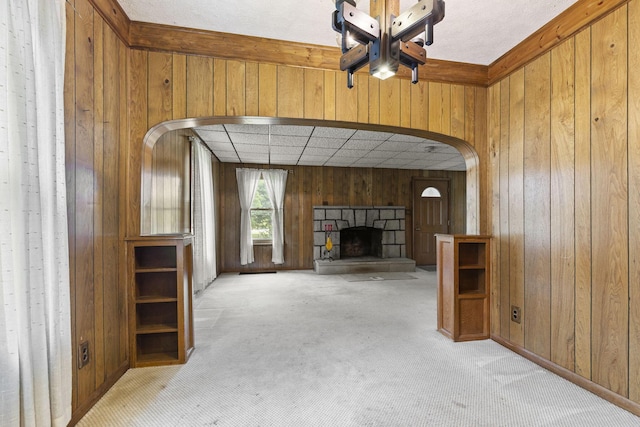 unfurnished living room featuring a fireplace, light colored carpet, and wood walls