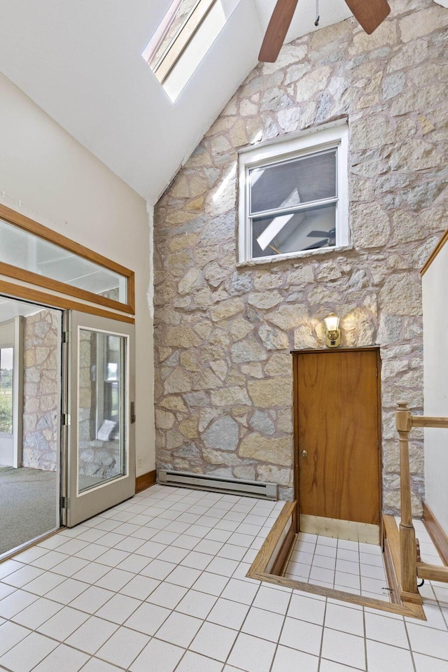 tiled foyer entrance featuring high vaulted ceiling, ceiling fan, a baseboard radiator, and a skylight