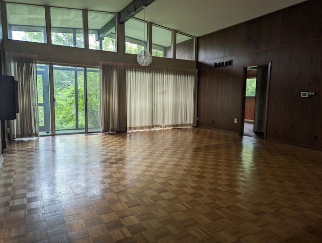 unfurnished living room with dark parquet floors, high vaulted ceiling, and wood walls