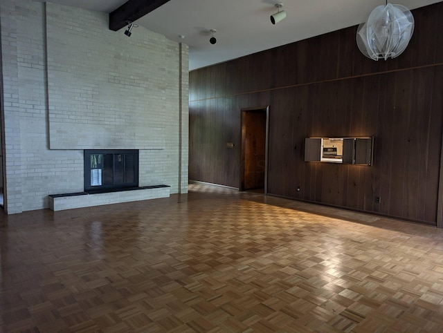 unfurnished living room with beam ceiling, wood walls, a towering ceiling, and a brick fireplace