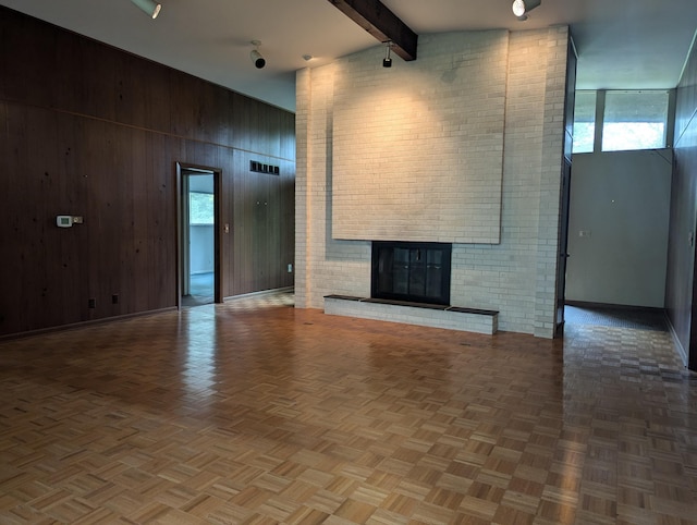 unfurnished living room featuring beamed ceiling, a healthy amount of sunlight, wood walls, and a fireplace