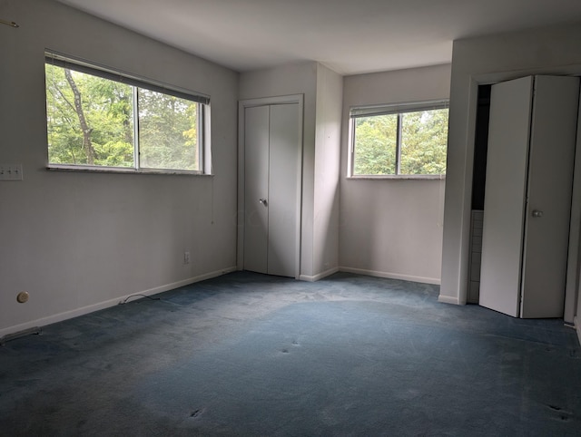 unfurnished bedroom with dark carpet, multiple windows, and multiple closets