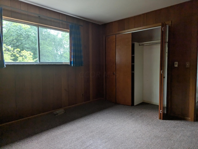 unfurnished bedroom featuring carpet flooring, wooden walls, and a closet