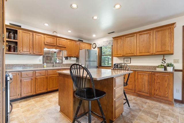 kitchen featuring a center island, sink, light stone countertops, appliances with stainless steel finishes, and a breakfast bar area