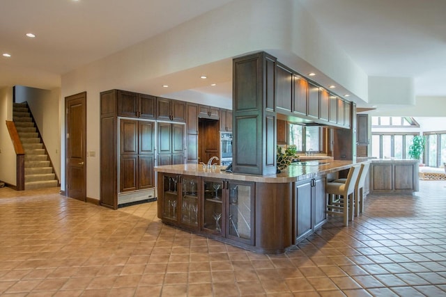 kitchen featuring a kitchen breakfast bar, dark brown cabinets, light tile patterned floors, a center island with sink, and oven