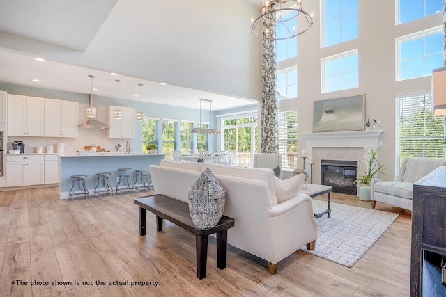 living room featuring a notable chandelier, light hardwood / wood-style floors, a towering ceiling, and a fireplace