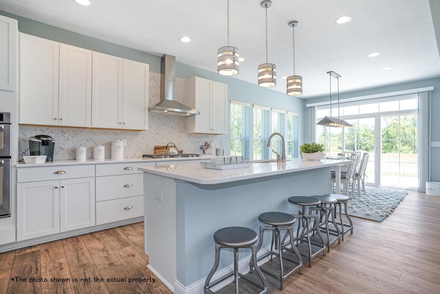 kitchen featuring white cabinets, a healthy amount of sunlight, wall chimney exhaust hood, and an island with sink