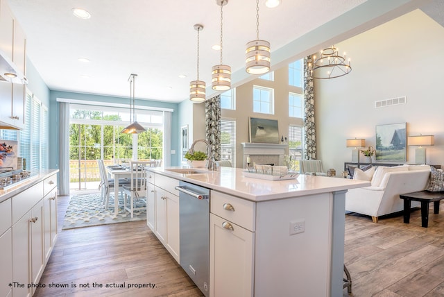 kitchen with a kitchen island with sink, light wood-type flooring, decorative light fixtures, white cabinetry, and a chandelier