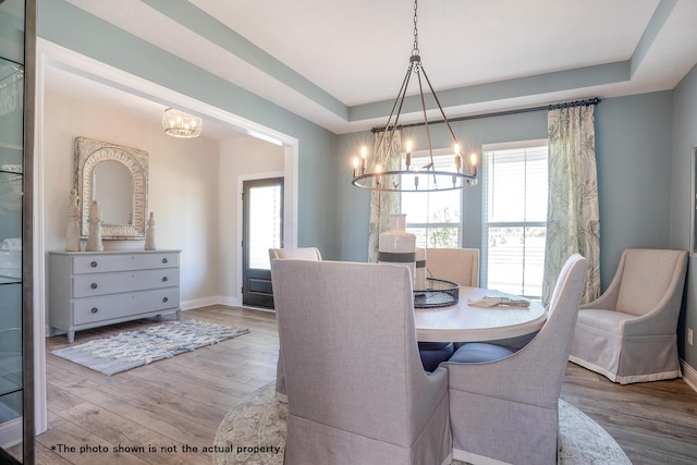 dining area with hardwood / wood-style floors, a raised ceiling, an inviting chandelier, and a wealth of natural light