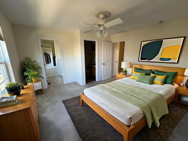 bedroom featuring washer / dryer, a walk in closet, ceiling fan, dark carpet, and ensuite bathroom