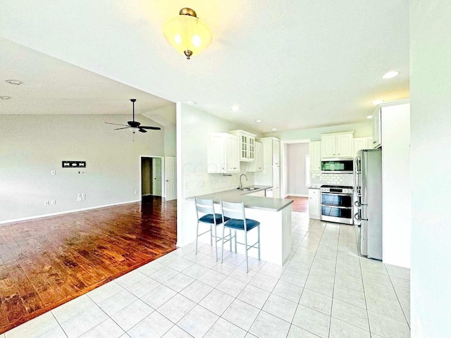 kitchen with white cabinets, vaulted ceiling, light wood-type flooring, appliances with stainless steel finishes, and kitchen peninsula