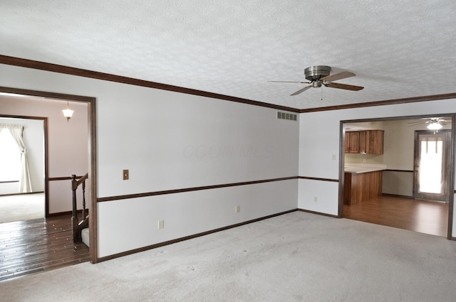 carpeted empty room featuring ceiling fan, crown molding, and a textured ceiling