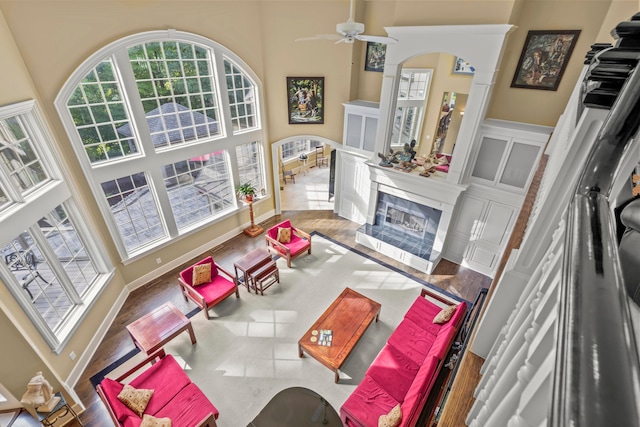 living room with ceiling fan, a fireplace, a towering ceiling, and wood-type flooring